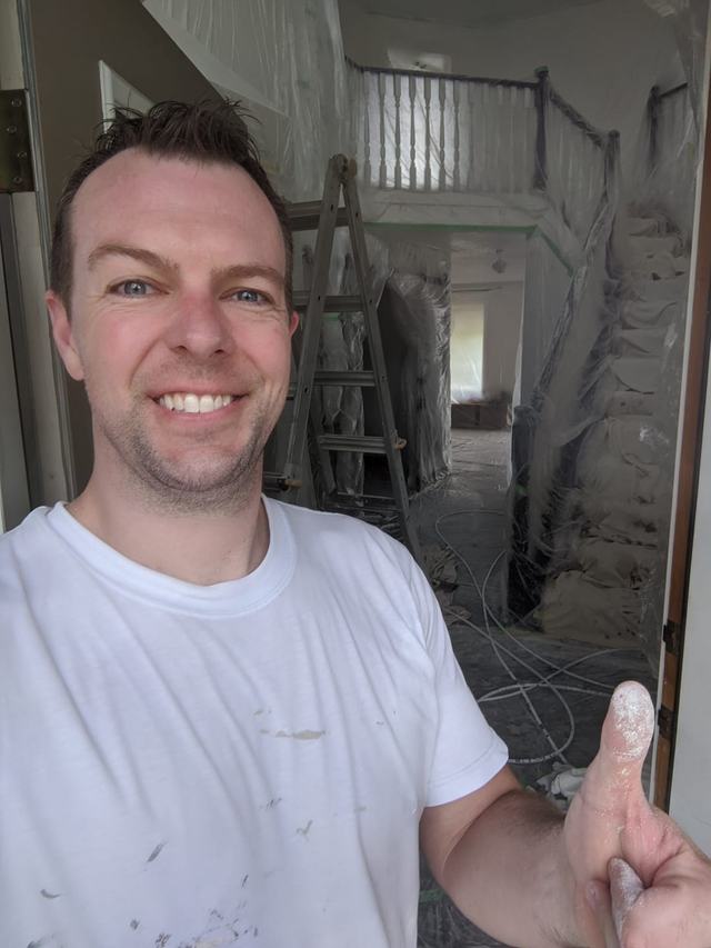 Justin smiling and giving a thumbs-up in front of a fully masked foyer and staircase ready for spraying