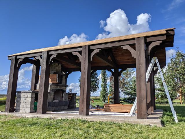 Large timber pergola and outdoor kitchen stained dark brown under a blue sky